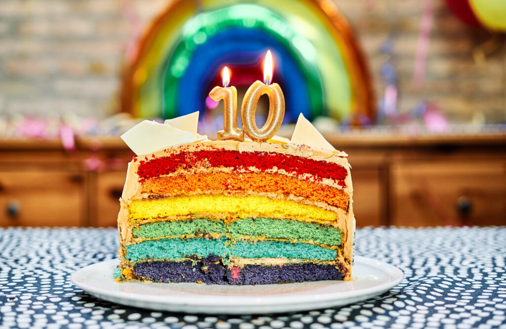 Rainbow coloured cake with candles in the shape of a 1 and 0.